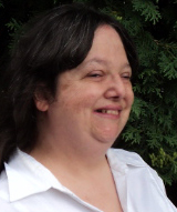 Head and shoulders photo of white woman smiling with dark brown hair combed back from her face, wearing a white blouse.