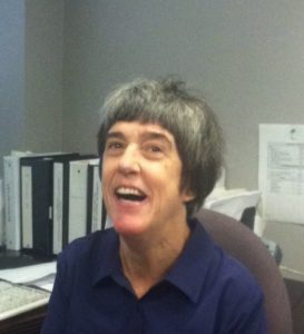 Photo of Lisa Blumberg, head and shoulders shot of a smiling woman with short gray hair and a dark blue blouse seated with a desk of files and books in the background.