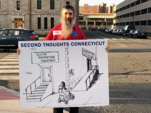 Second Thoughts CT member Stephen Mendelsohn holds displaying cartoon of stairs to suicide prevention and a ramp to assisted suicide