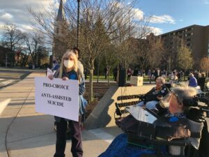Second Thoughts CT member Joan Cavanagh holds "Pro-Choice/Anti-Assisted Suicide" sign near protesters in wheelchairs