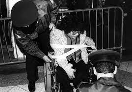 Lillibeth Navarro arrested by two officers while strapped in her wheelchair near a police barricade.